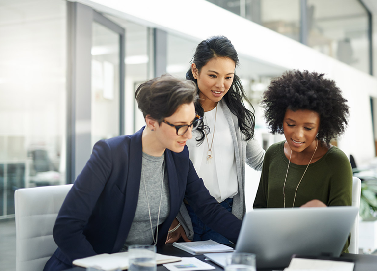 Three colleagues collaborate around a laptop reviewing documents